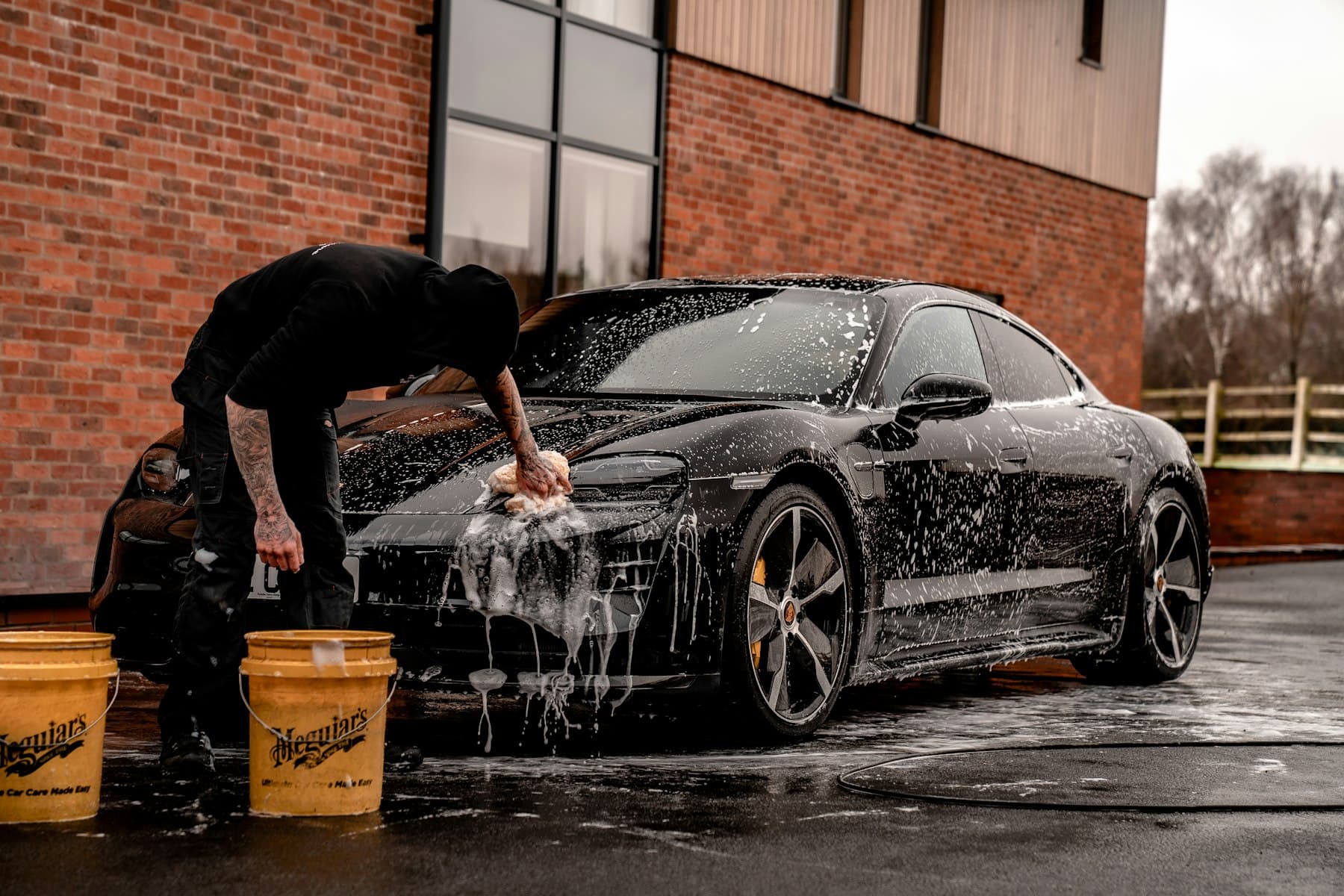 Profissional lavando um carro preto coberto de espuma